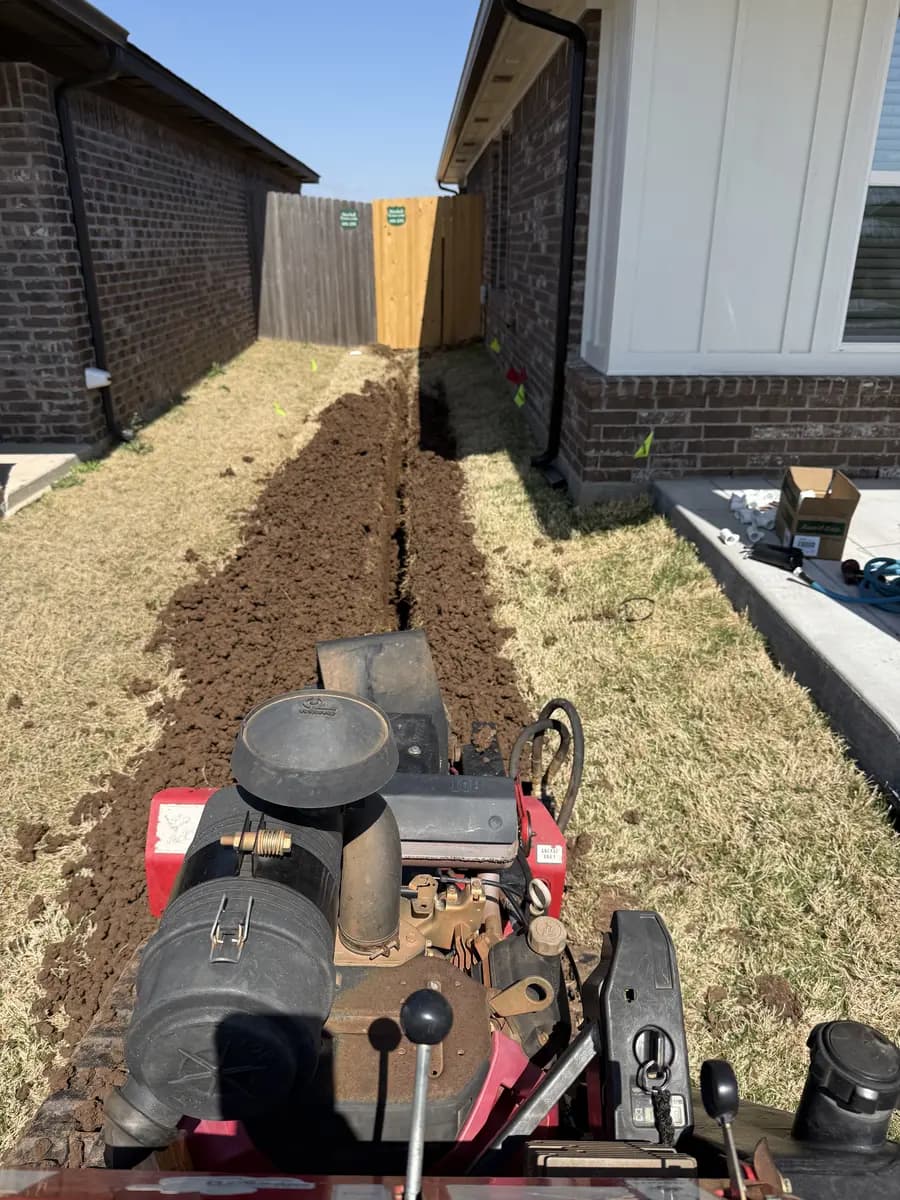 Trenching machine cutting a drainage route beside a residential home