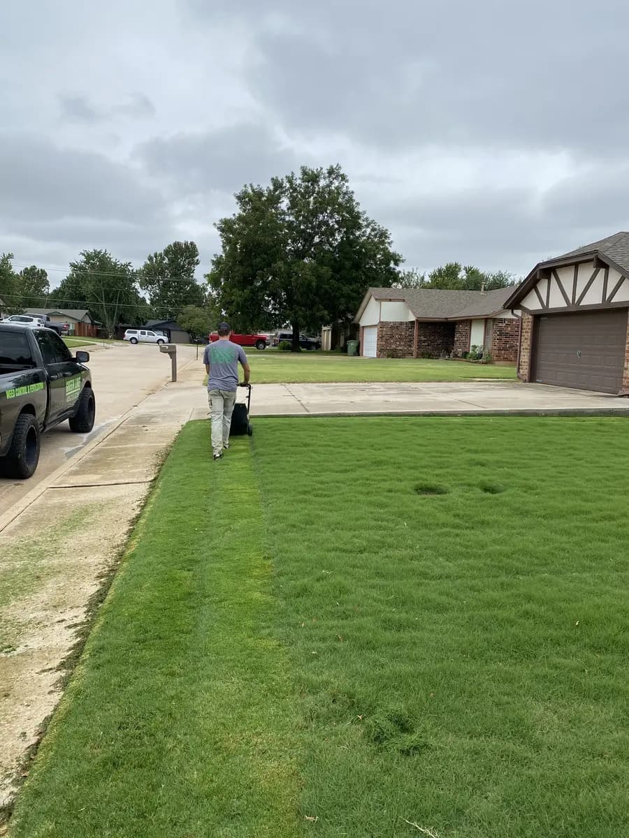 Greenline crew member pushing a walk-behind mower across a residential front lawn