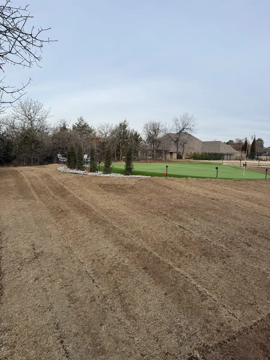 Broad prepared soil area with parallel rows surrounding a backyard putting green before lawn establishment